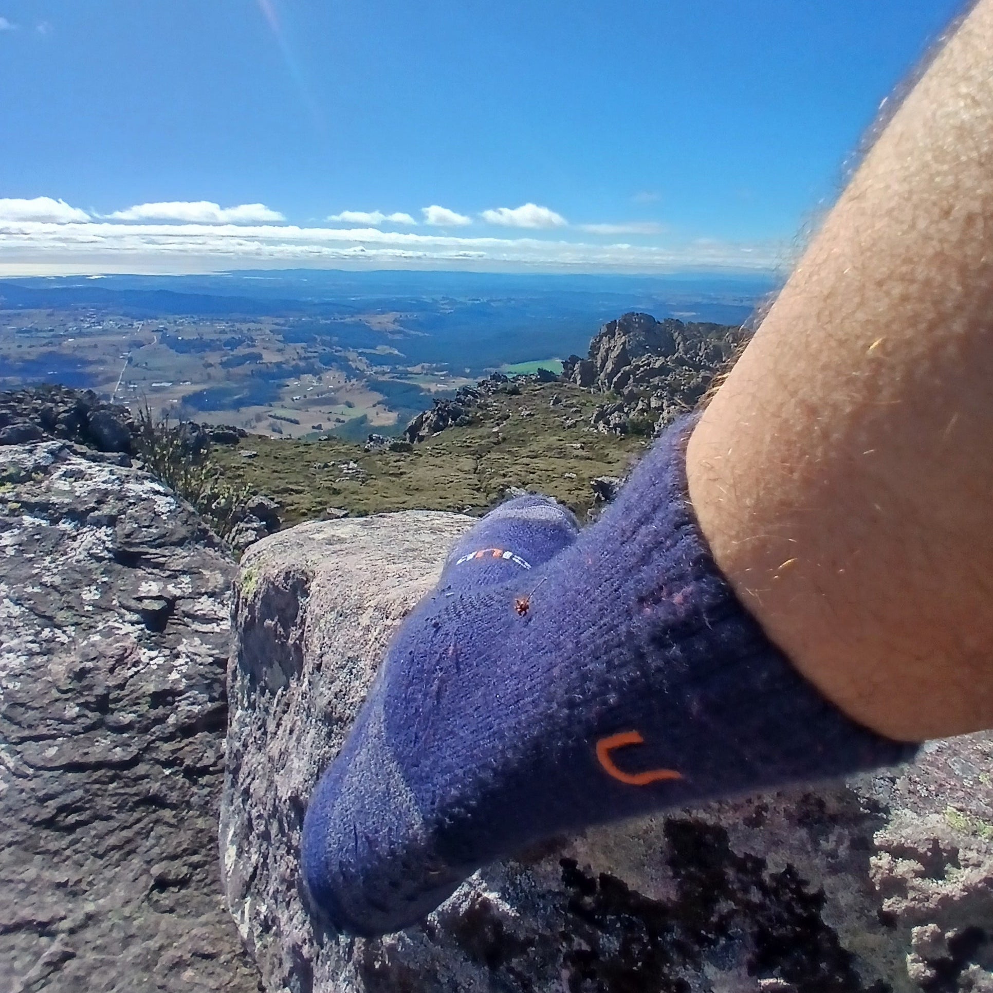 Person wearing blue socks with a logo, standing on a rocky cliff on top of a mountain