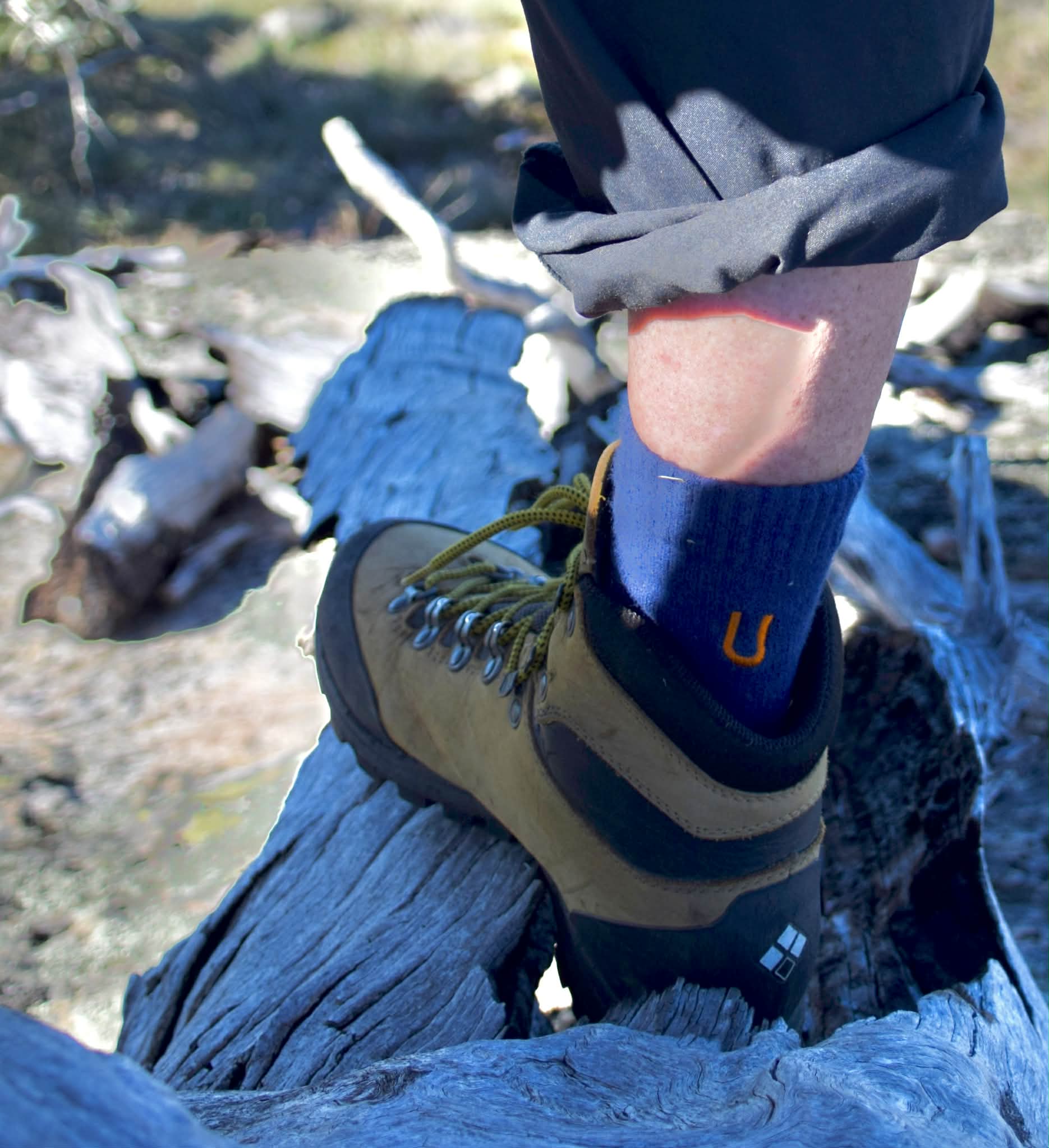 Person wearing a blue sock with a 'U' logo and a hiking boot in a natural setting.