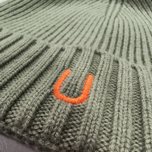 Close-up of front of 100% merino wool eucalyptus green ribbed knit beanie with bright orange embroidered U logo, showing fine texture and stitching detail
